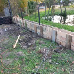 Deskowanie fundamentów domu w trakcie budowy, widoczne zbrojenie i szalunek drewniany, w tle staw.