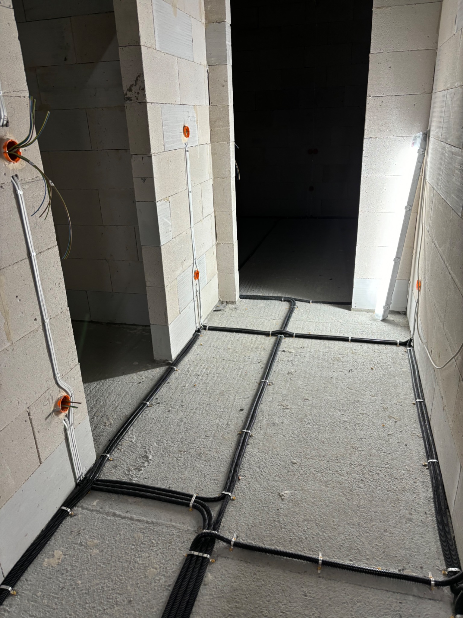Wnętrze w trakcie prac elektrycznych: kable w peszlach ułożone na podłodze, prowadzące do puszek instalacyjnych w ścianach z betonu komórkowego.