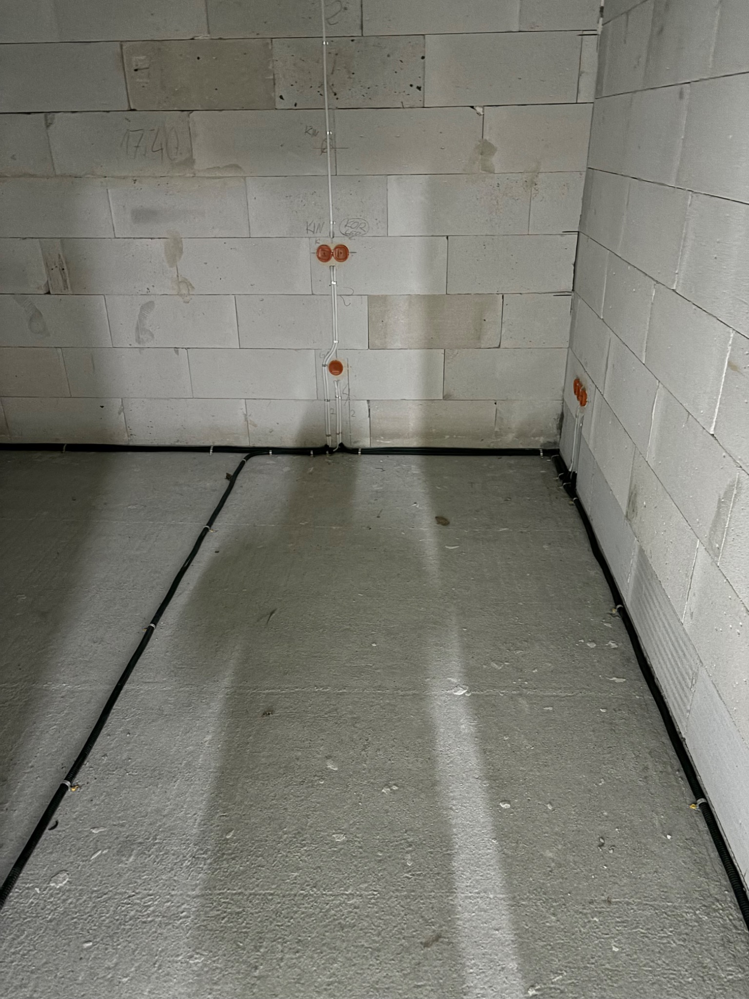 Surowy stan: kable elektryczne w peszlach prowadzone wzdłuż ściany z betonu komórkowego, puszki instalacyjne w ścianie, przewody wyprowadzone z puszek pionowo w górę.