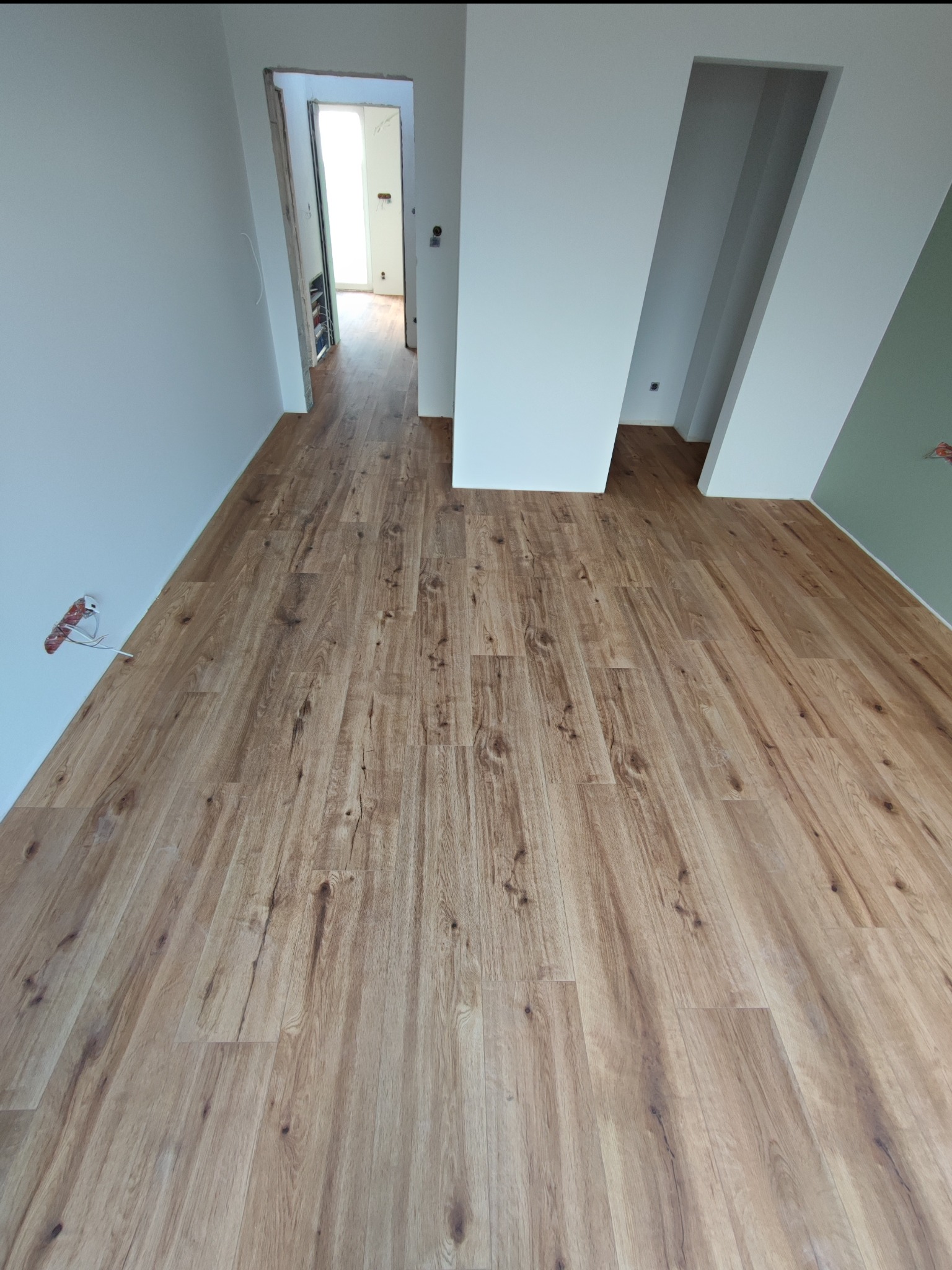 Nowo położona, jasna podłoga imitująca drewno w pustym pomieszczeniu w Lublinie, z widocznymi niedokończonymi elementami instalacji elektrycznej przy ścianie.