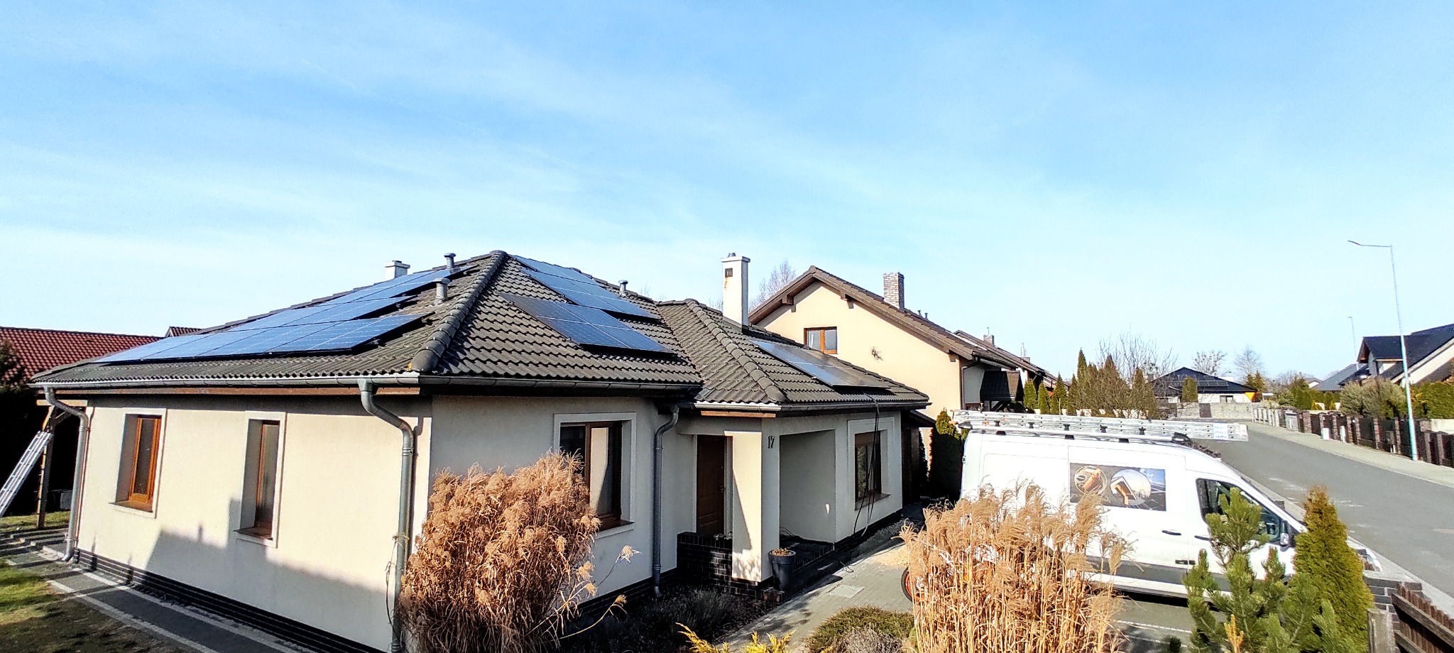 Dom jednorodzinny z panelami słonecznymi na dachu, widoczny z perspektywy ulicy, z samochodem serwisowym zaparkowanym obok.