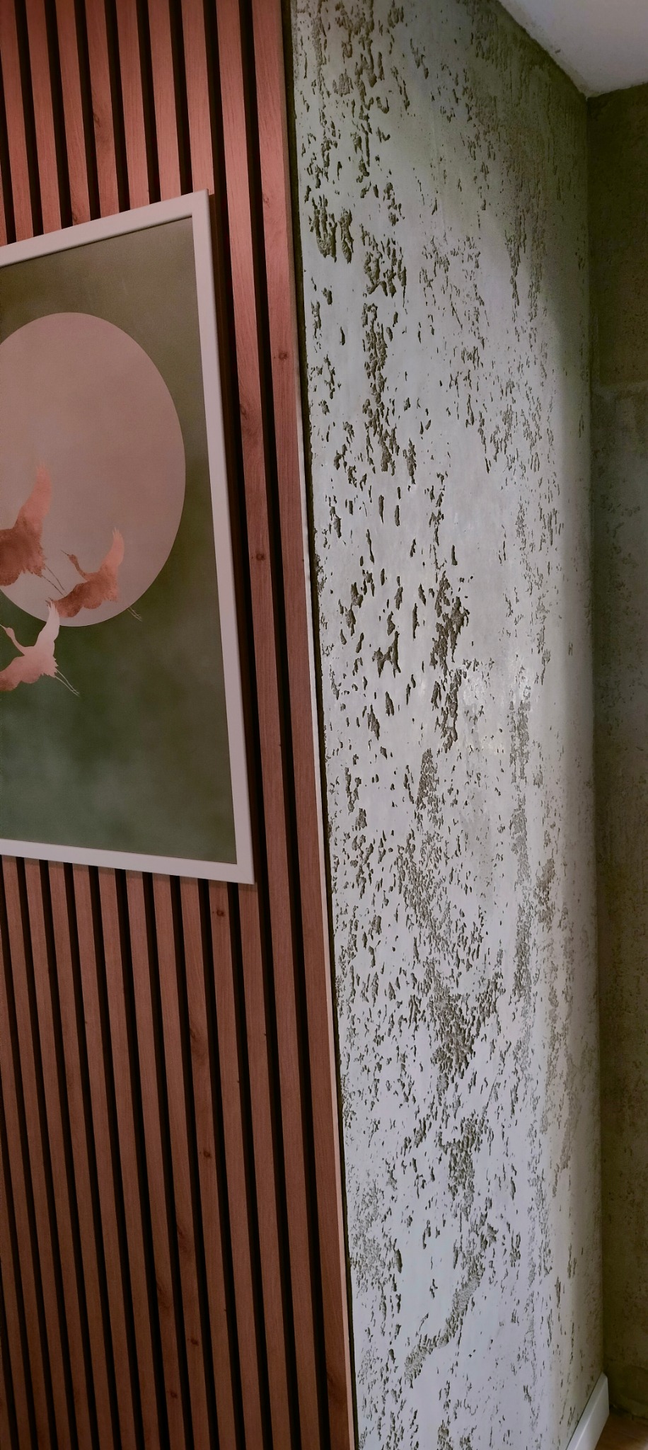 Dekoracyjna ściana z efektem spękań i drewniane lamele z obrazem w ramie. Nietypowe wykończenie wnętrza, akcentujące nowoczesny design.