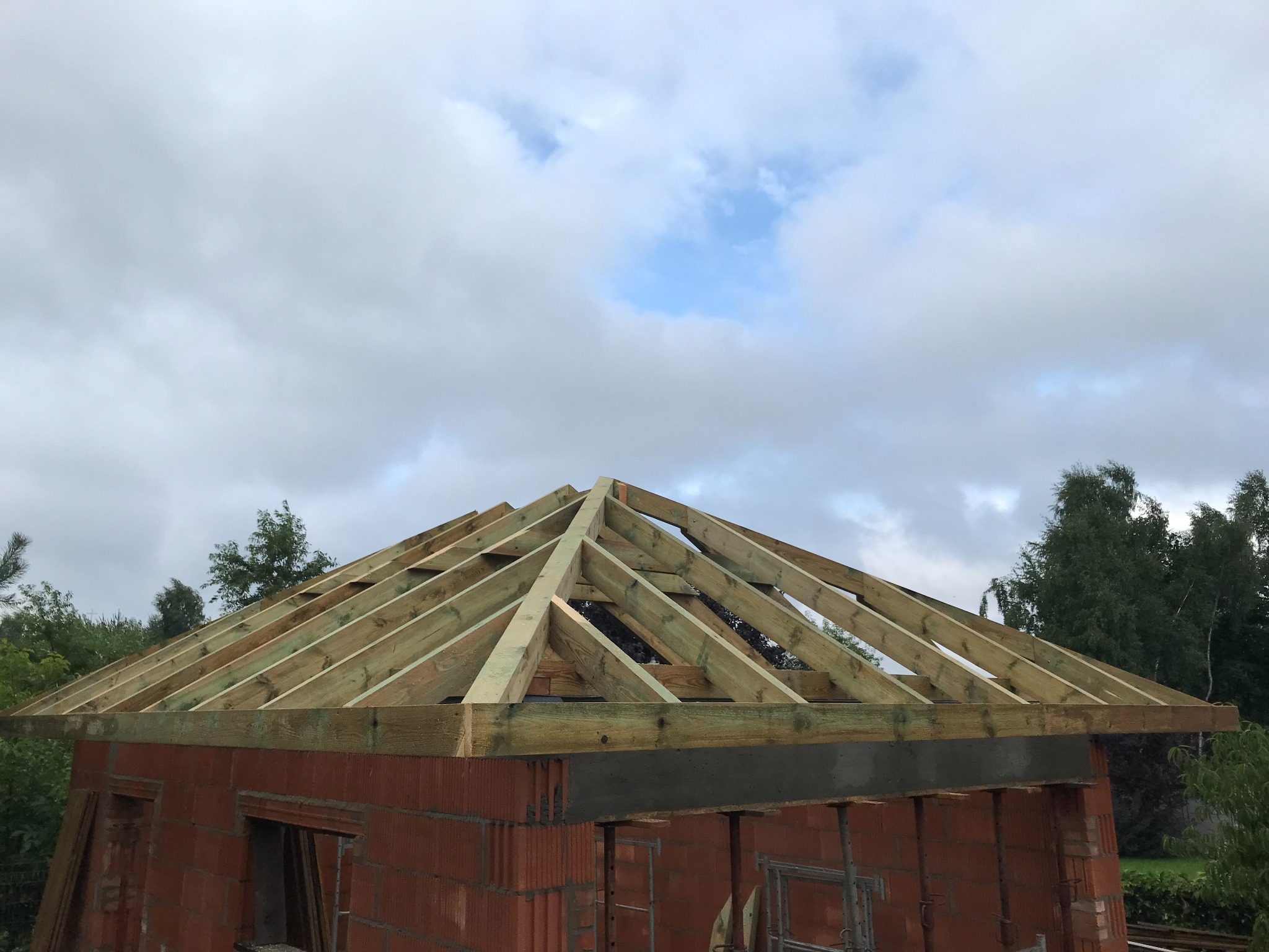 Wznoszenie drewnianej konstrukcji dachu na budynku z czerwonej cegły, widok na niebo z chmurami.