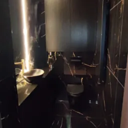 Elegancka łazienka wykończona czarnym marmurem z złotymi żyłami, z podświetlanym lustrem i umywalką nablatową, widok z perspektywy wejścia.