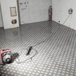 RBTS Usługi Ogólnobudowlane Robert Szczepańczyk - Świeżo ułożona, wzorzysta podłoga z płytek w łazience w trakcie remontu, widoczne narzędzia glazurnicze i nieukończone ściany z wystającymi kablami.