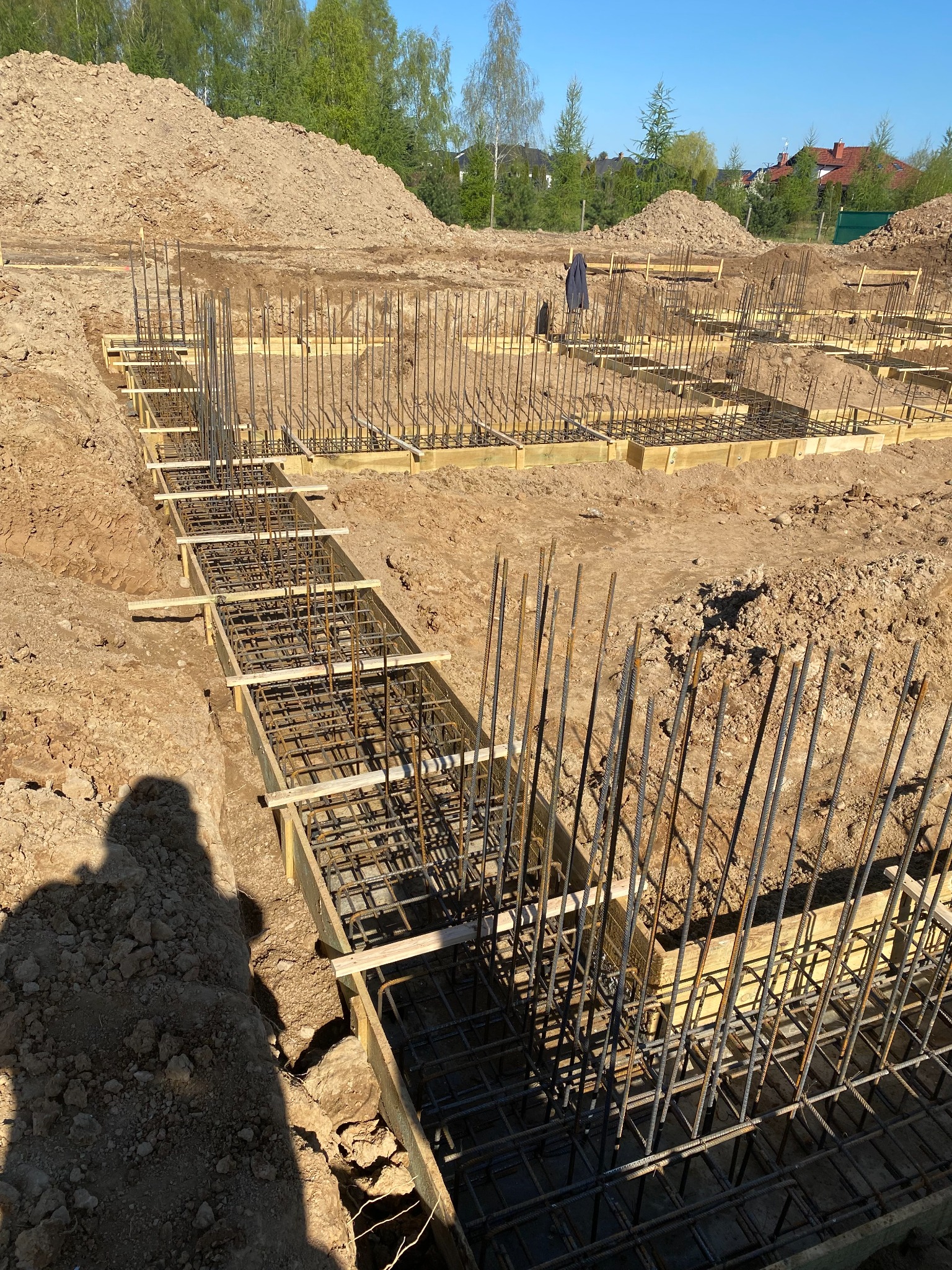 Zbrojenie i szalunek pod wylewkę fundamentów domu jednorodzinnego, widoczny cień osoby fotografującej w lewym dolnym rogu.