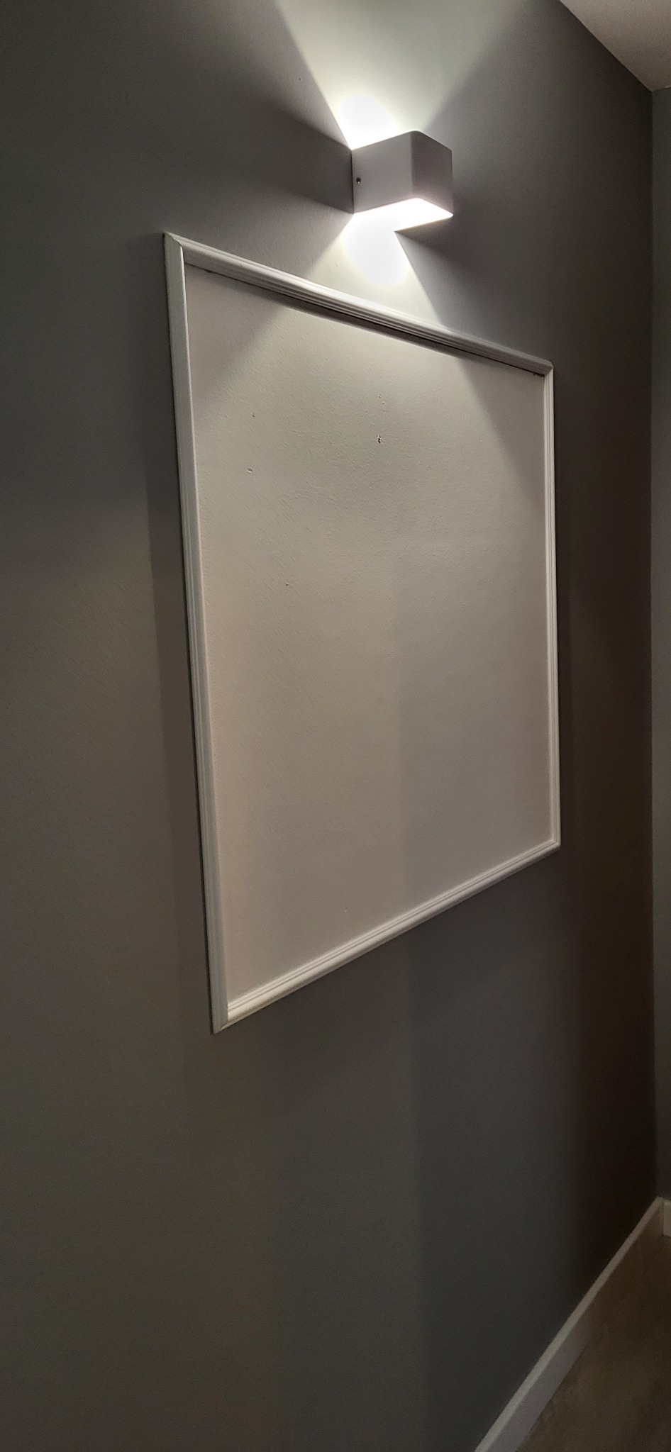 Świeżo zamontowana płyta kartonowo-gipsowa z widoczną białą ramą, umieszczona na szarej ścianie pod nowoczesnym oświetleniem punktowym.