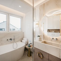 ALL DESIGN INSIDE Aleksandra Lepka - Elegancka łazienka w bieli i beżu z marmurowymi akcentami. Wolnostojąca wanna, okrągłe lustro z podświetleniem LED i designerska umywalka tworzą luksusowy klimat.