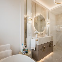 ALL DESIGN INSIDE Aleksandra Lepka - Elegancka łazienka w odcieniach beżu i bieli. Okrągłe lustro z podświetleniem LED nad umywalką. Marmurowe wykończenie ścian i podłogi. Luksusowe oświetlenie.