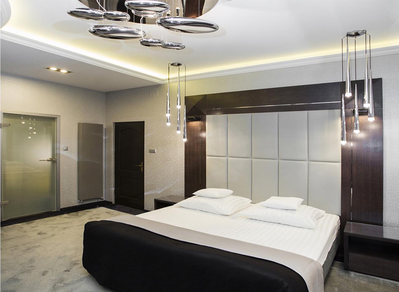 Nowoczesna sypialnia z dużym łóżkiem, tapicerowanym zagłówkiem, srebrnymi lampami wiszącymi i lustrzanym sufitem z oświetleniem LED.
