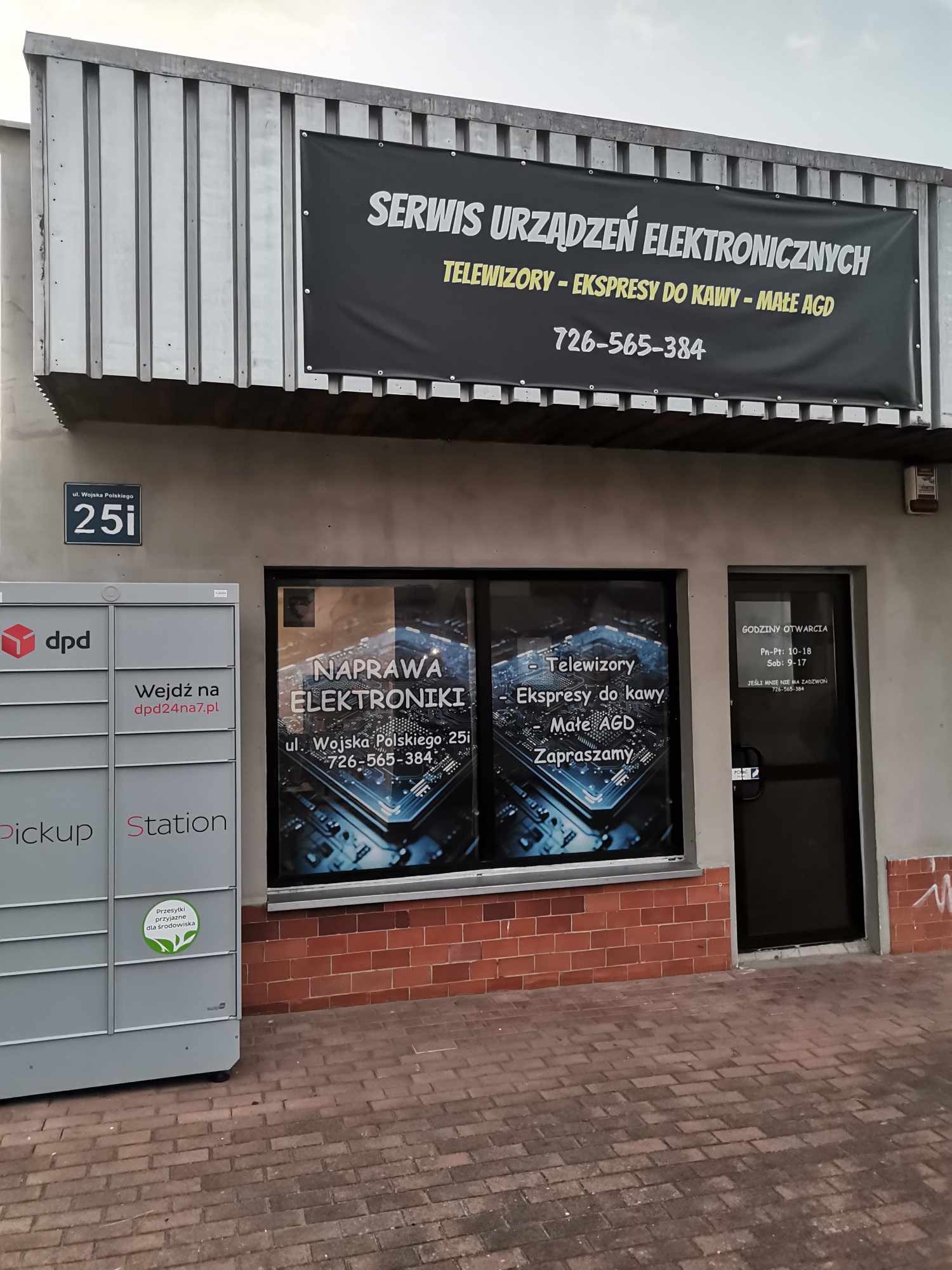 Fasada budynku z szyldem 'Serwis Urządzeń Elektronicznych' i naklejkami na oknach informującymi o naprawie elektroniki, w tym telewizorów, ekspresów do kawy i małego AGD, obok paczkomat DPD.