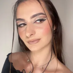 Portret kobiety z wyrazistym, wieczorowym w odcieniach beżu i czerni, z podkreślonymi brwiami i delikatnym r&oacute;żem na policzkach, uzupełnionym srebrną biżuterią.