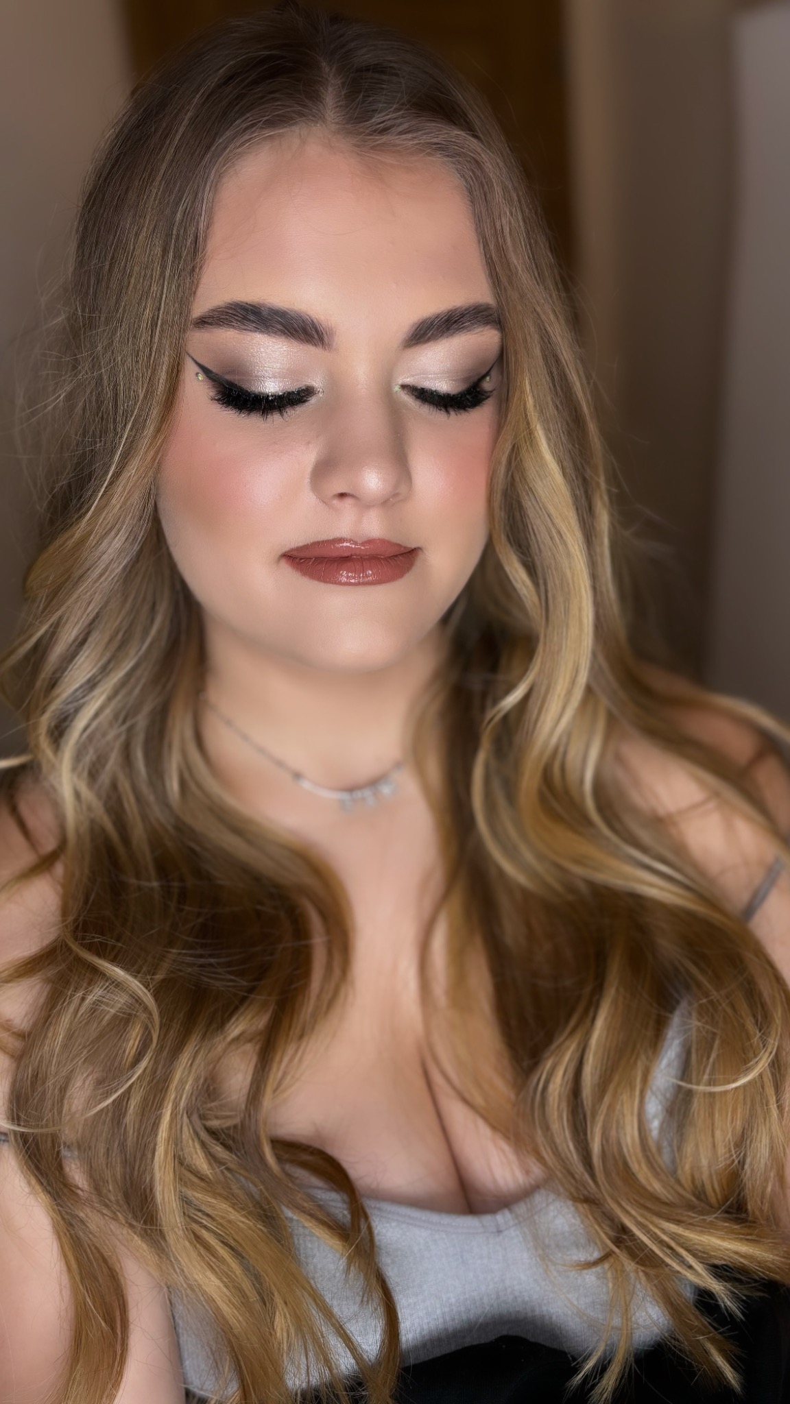 Portret kobiety z zamkniętymi oczami, prezentującej delikatny, błyszczący cień na powiekach z czarną kreską, podkreślone brwi i usta w kolorze nude, z blond włosami opadającymi na ramiona.