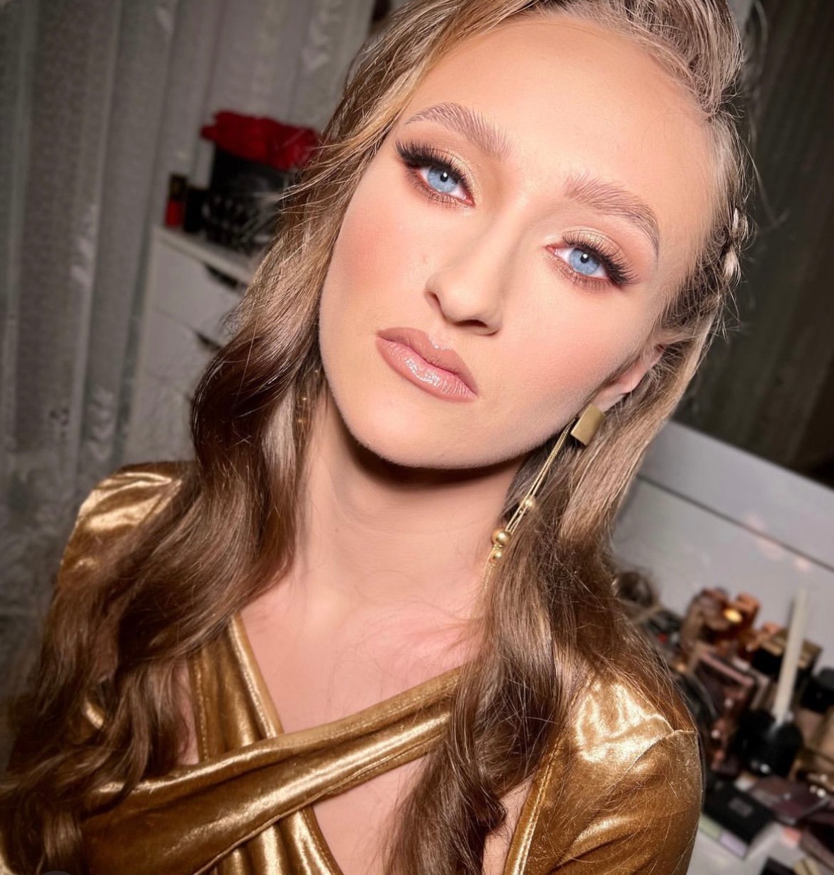 Portret kobiety z profesjonalnie wykonanym, subtelnym makijażem w odcieniach brązu i złota, podkreślającym niebieskie oczy. Uwagę zwracają długie, gęste rzęsy i błyszczące usta. Włosy ułożone...