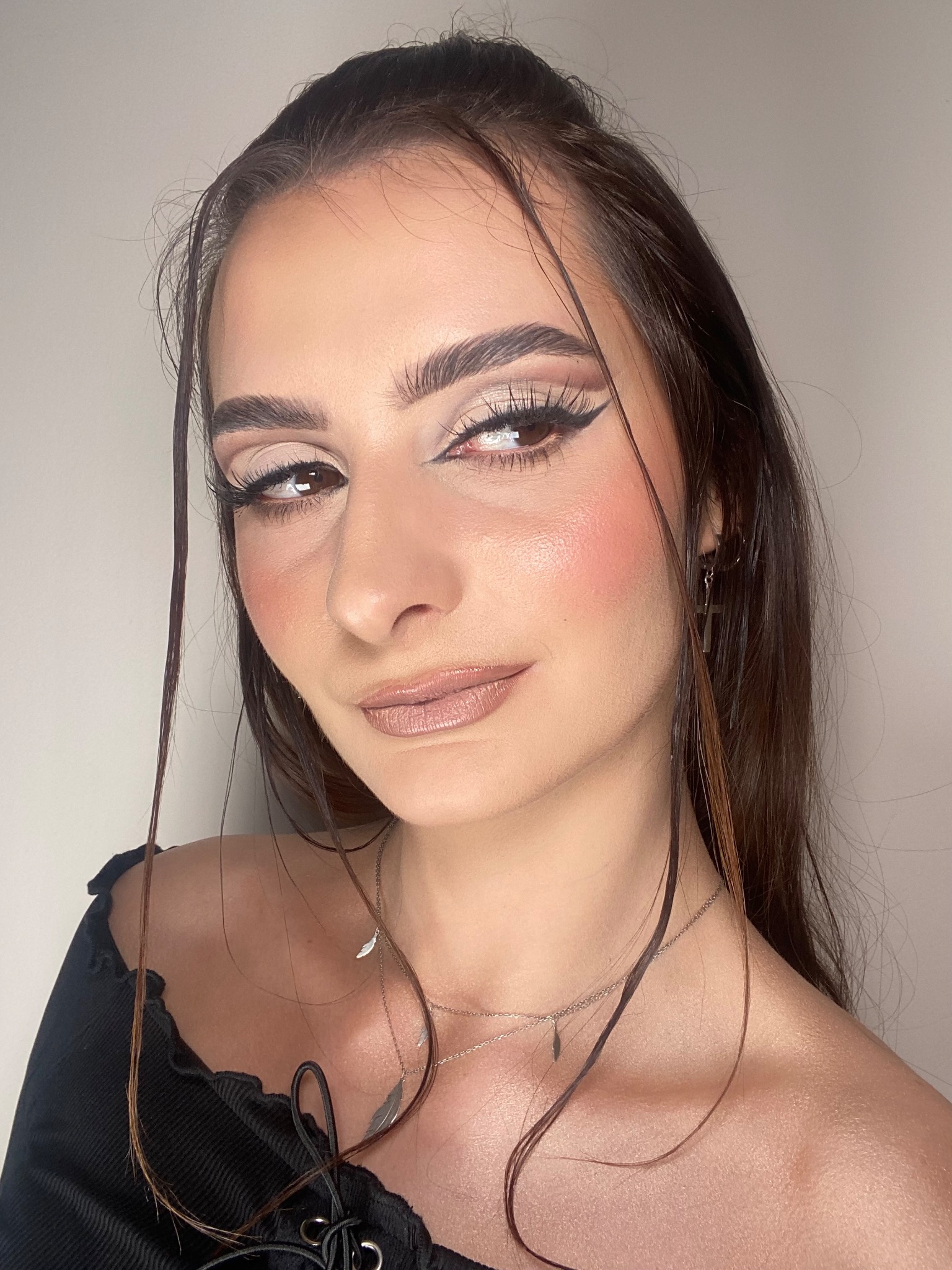 Portret kobiety z wyrazistym, wieczorowym w odcieniach beżu i czerni, z podkreślonymi brwiami i delikatnym różem na policzkach, uzupełnionym srebrną biżuterią.