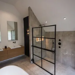 Nowoczesna łazienka z kabiną prysznicową w stylu loft, szara płytka imitująca beton, drewniana szafka pod umywalką i czarne akcenty armatury.