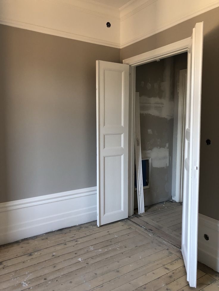 Pokój po malowaniu ścian na szaro, z odrestaurowaną drewnianą podłogą i otwartymi białymi drzwiami, widoczne ślady prac remontowych w sąsiednim pomieszczeniu.