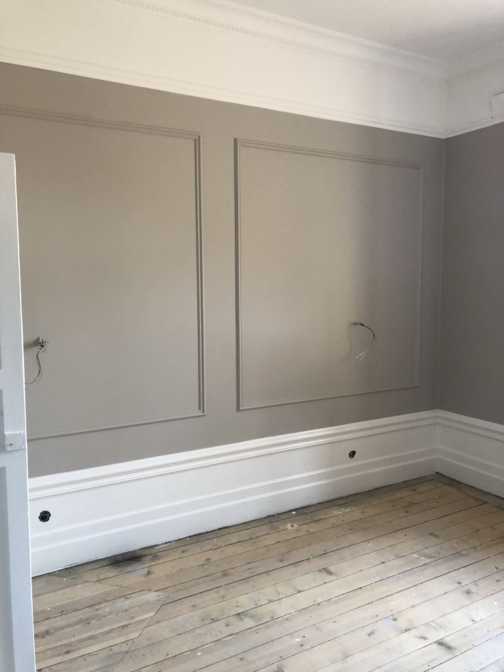 Pokój po remoncie z szarymi ścianami z dekoracyjnymi panelami, białymi listwami przypodłogowymi i sufitem oraz drewnianą podłogą; widoczne wystające kable elektryczne