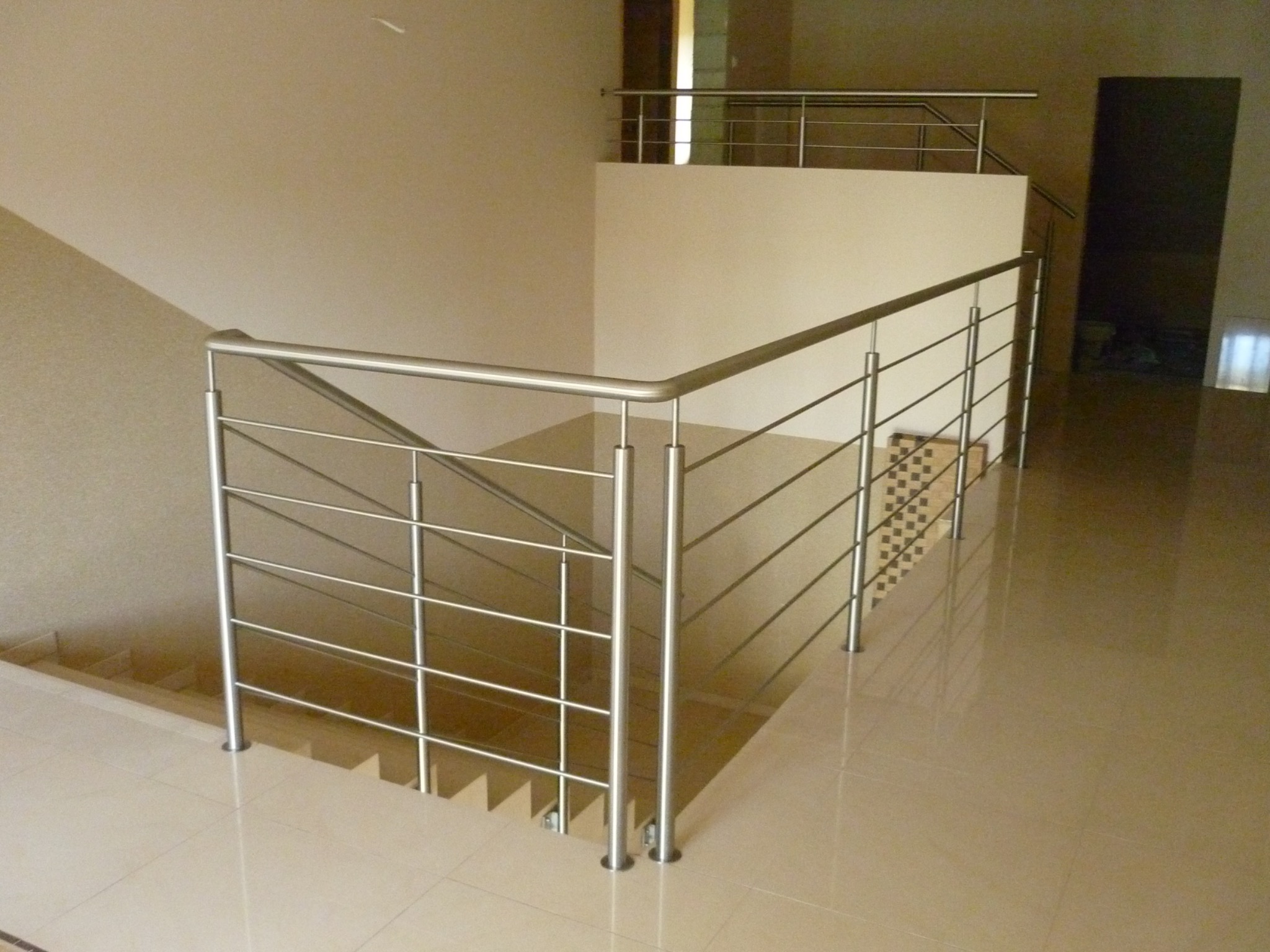 Nowoczesna, metalowa balustrada z poziomymi prętami, zamontowana na schodach i antresoli w jasnym wnętrzu.