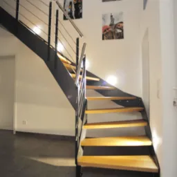 Nowoczesne schody z drewnianymi stopniami, czarną konstrukcją i metalową balustradą w jasnym wnętrzu z dekoracjami ściennymi.