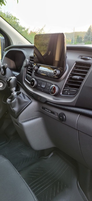 Wnętrze kabiny busa z widoczną deską rozdzielczą, dźwignią zmiany biegów i gumowymi dywanikami podłogowymi.