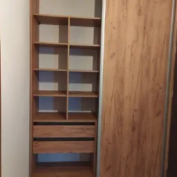 Wnętrze szafy przesuwnej z drewnopodobnymi frontami, widoczne półki i szuflady, oświetlenie naturalne, z bliska.