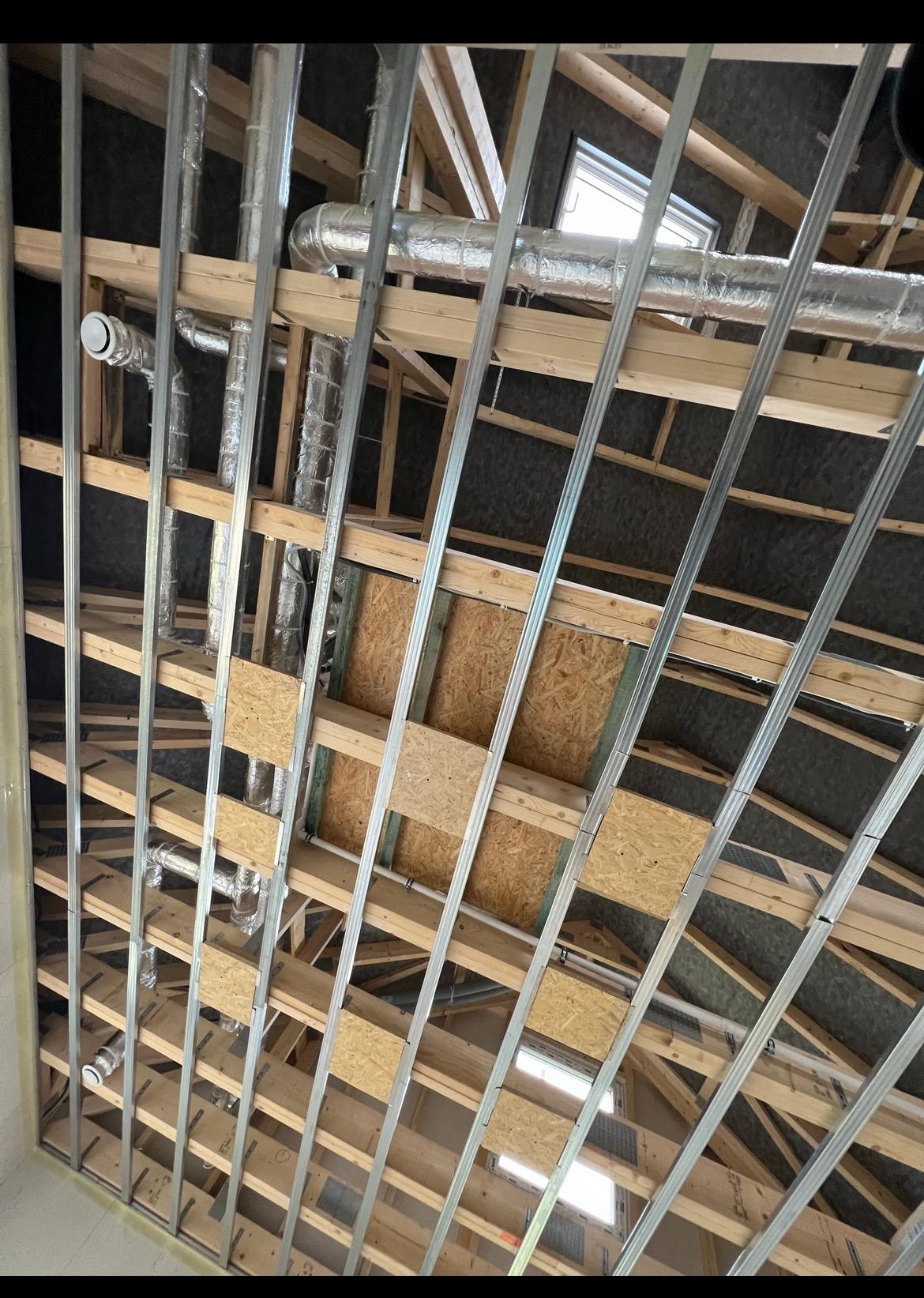 Konstrukcja drewniana poddasza z instalacją wentylacyjną i metalowymi profilami, widoczne okna dachowe i płyty OSB, etap prac wykończeniowych.