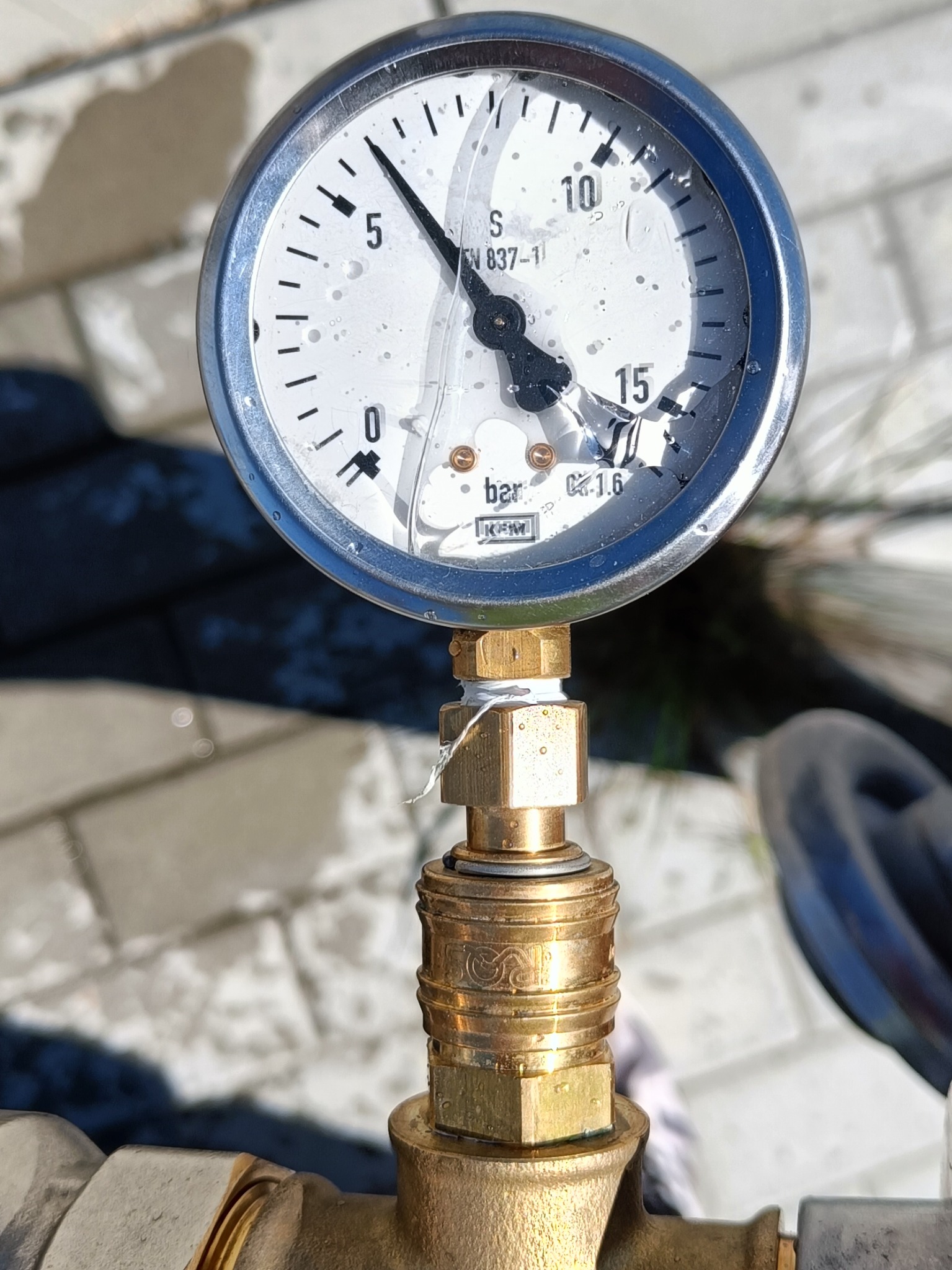 Manometr wskazujący ciśnienie, z pękniętą szybką i widocznymi śladami użytkowania, zamontowany na mosiężnej złączce.