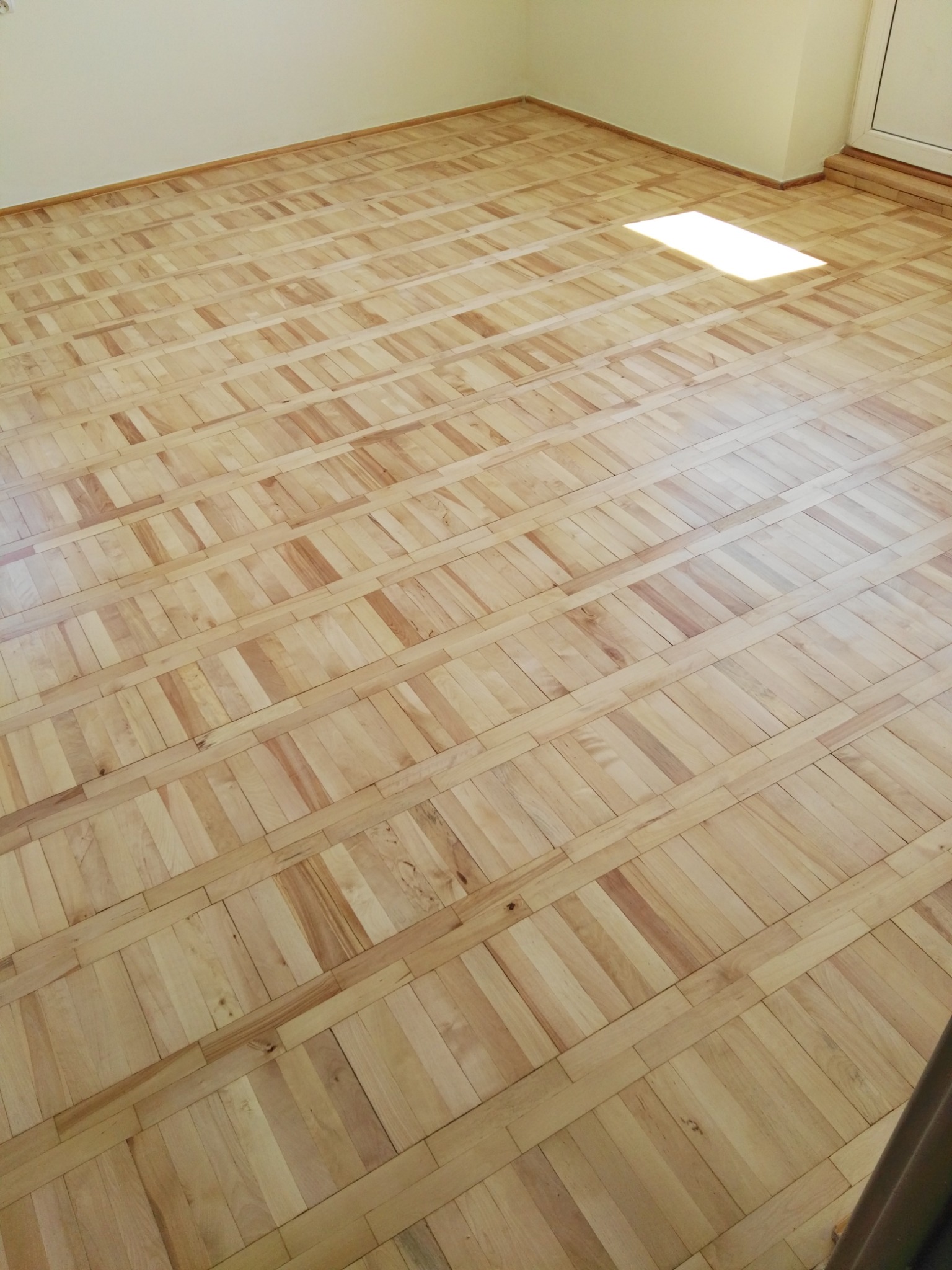 Ułożona parkietowa podłoga z jasnego drewna w pustym pokoju, oświetlona smugą światła słonecznego.