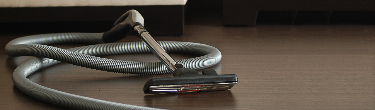 Szara rura i chromowana końcówka ssąca systemu centralnego odkurzania leżą na panelach podłogowych.