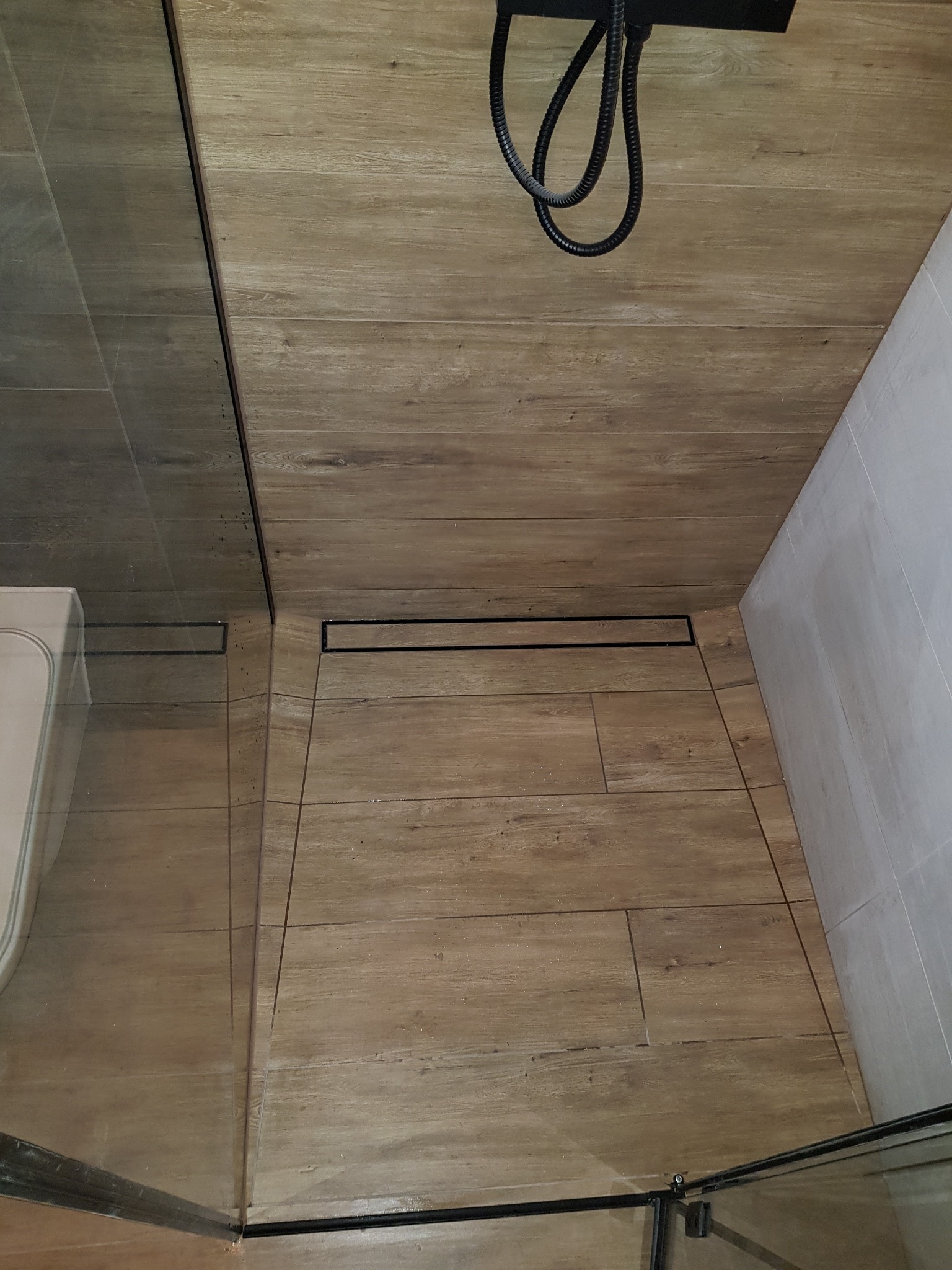 Kabina prysznicowa z odpływem liniowym w podłodze wyłożonej płytkami imitującymi drewno, widok z góry.