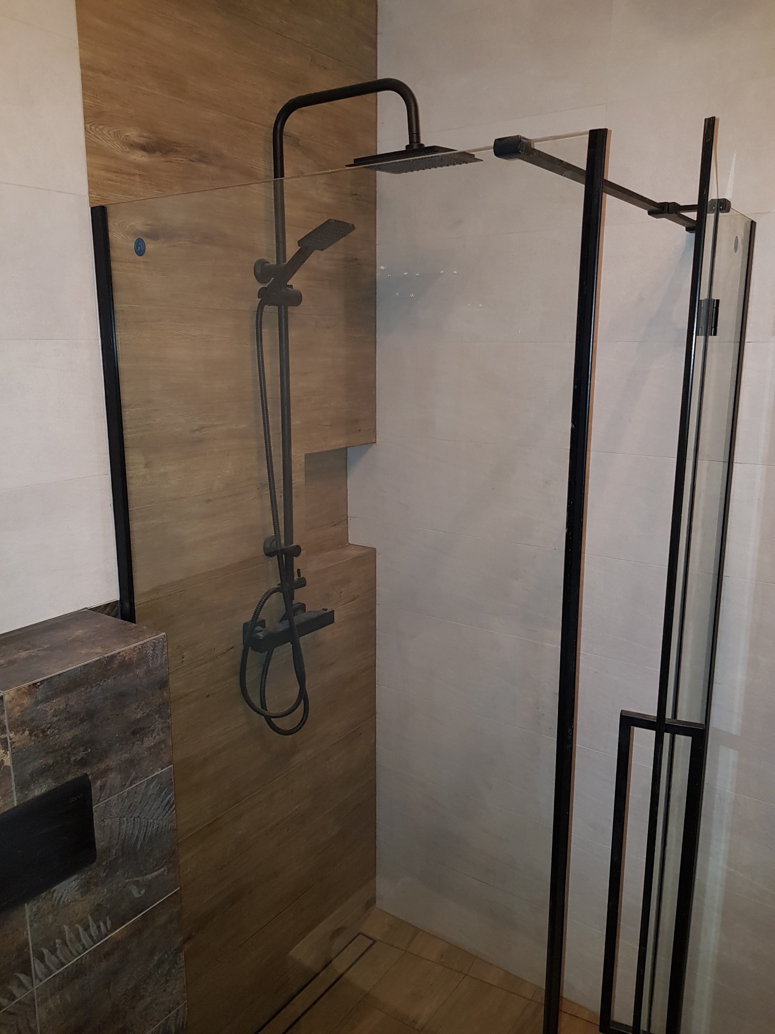 Nowoczesna kabina prysznicowa z czarną armaturą i drewnopodobnymi płytkami na ścianie.