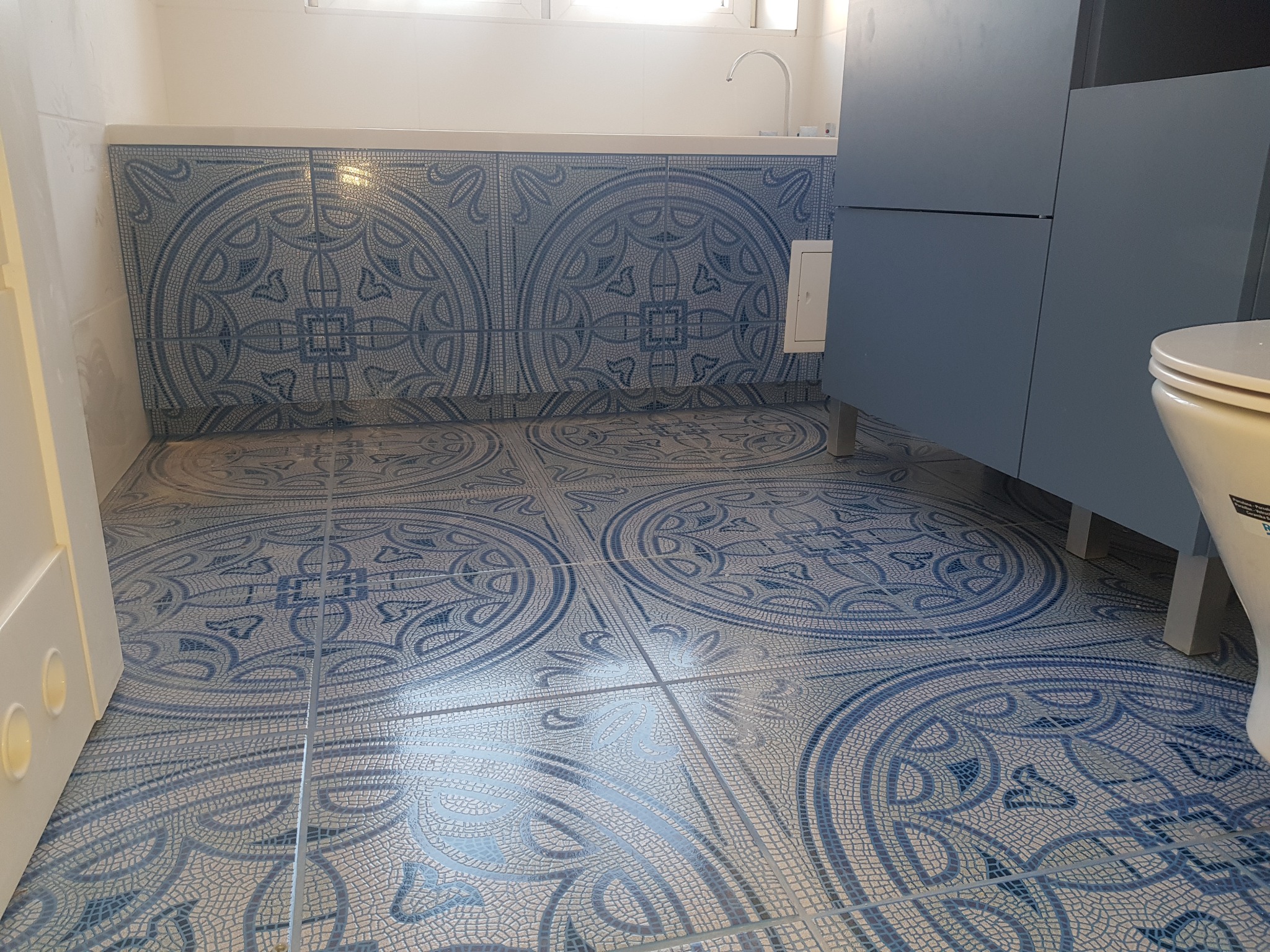 Wykończona łazienka z niebiesko-białymi płytkami podłogowymi i ściennymi z motywem mozaiki, widoczne elementy armatury i szafka pod umywalką.