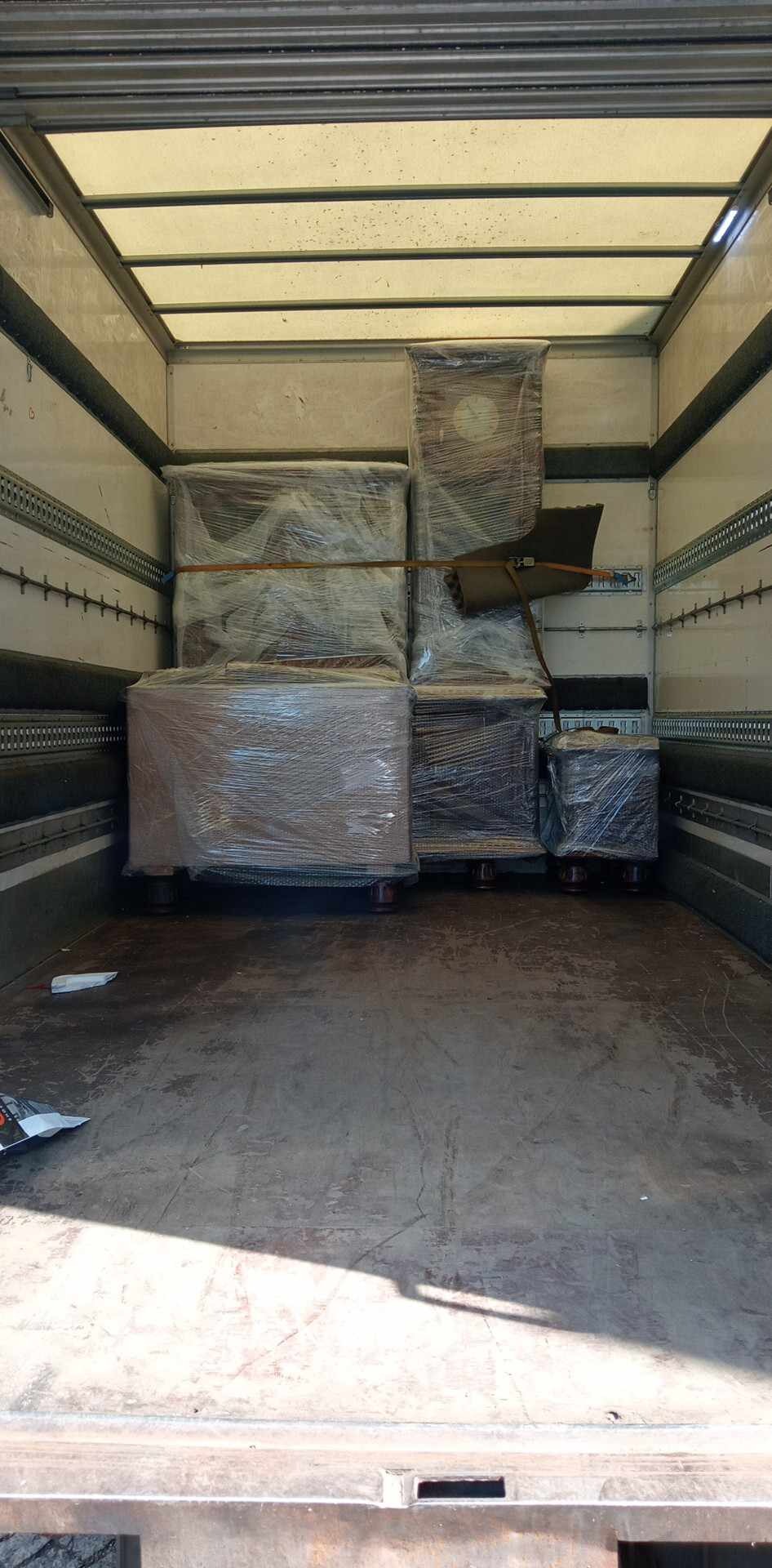 Wnętrze furgonetki z meblami zabezpieczonymi folią stretch i pasami transportowymi, gotowymi do przewozu.