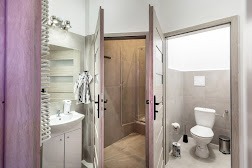 Jasna łazienka z umywalką, grzejnikiem drabinkowym, otwartymi drzwiami do kabiny prysznicowej i toalety z podwieszaną miską WC.