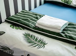 Łóżko w pokoju z niebieskim prześcieradłem i pościelą w motywy roślinne, na nim złożone białe ręczniki.