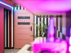 Różowe drzwi z symbolem toalety damskiej w nowoczesnym wnętrzu SPA z czarno-białymi pasami na ścianie i neonowym oświetleniem.