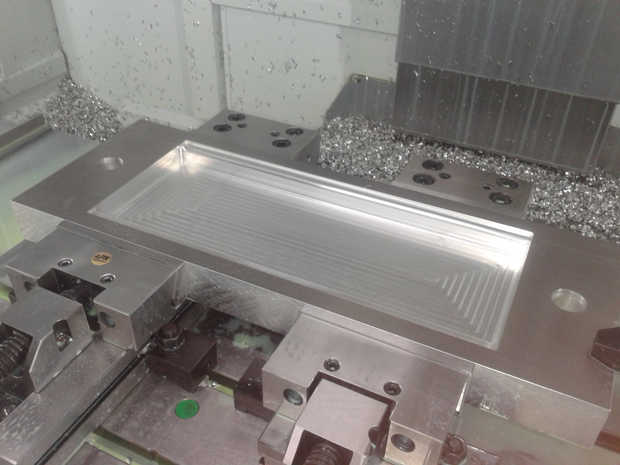 Obróbka metalu na frezarce CNC: Wyfrezowany prostokątny kształt w metalowym bloku, widoczne wióry i uchwyty mocujące.