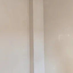 Wnętrze w trakcie prac wykończeniowych: fragment ściany z nałożoną warstwą gładzi, widoczne nierówności i ślady po szpachlowaniu, przygotowane do dalszej obróbki.