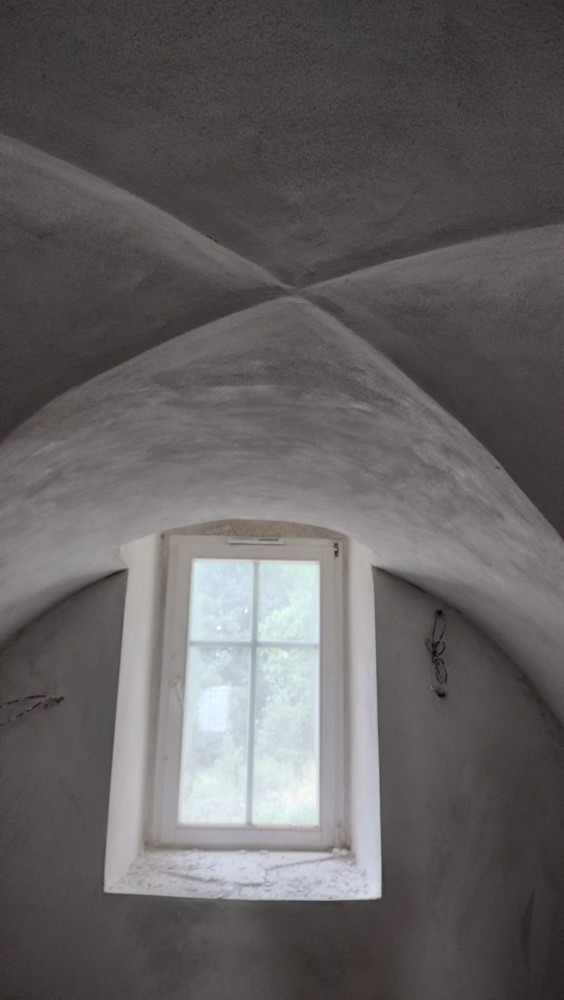 Kopułowy sufit z widocznym oknem w trakcie prac wykończeniowych, szary kolor ścian i sufitu, widoczne ślady po instalacjach elektrycznych.