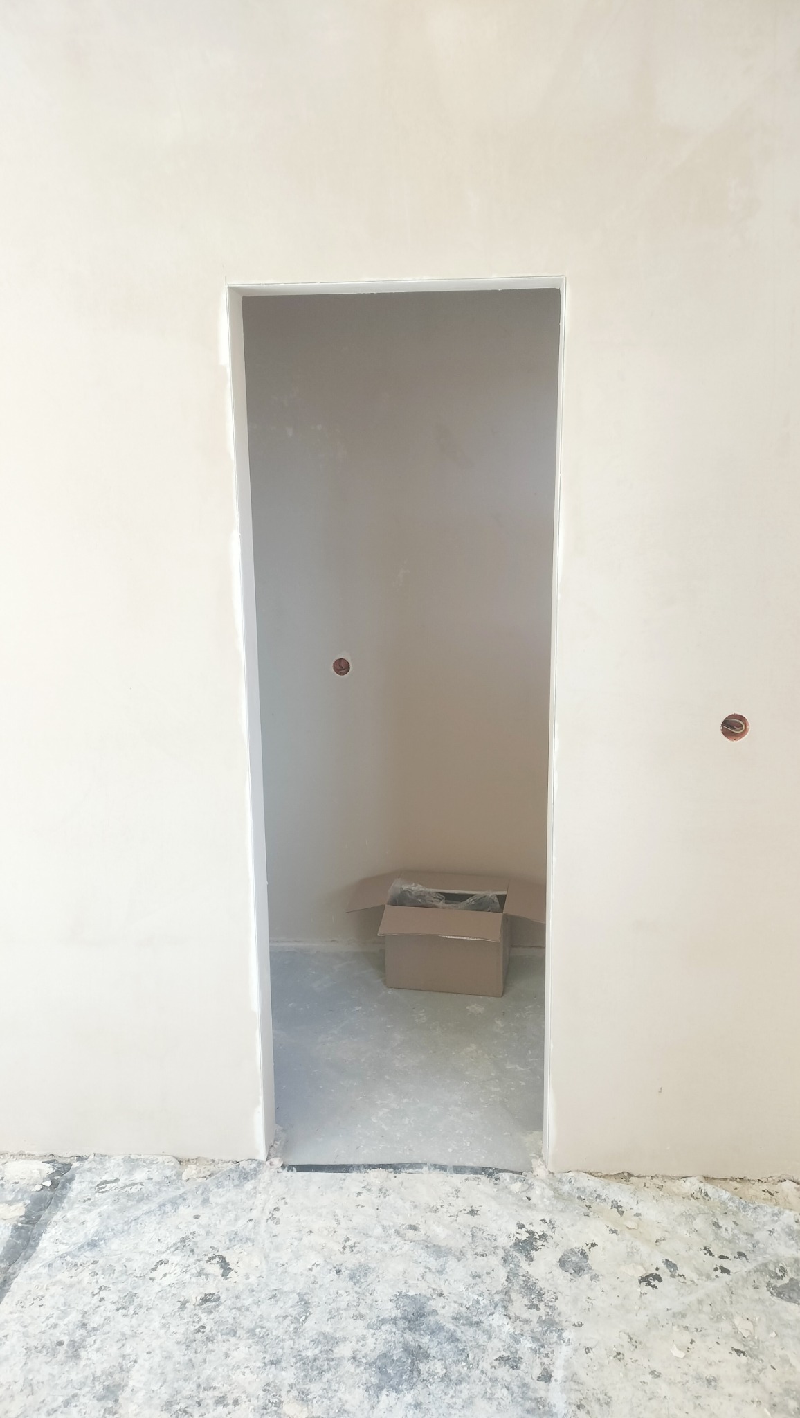 Wnętrze po nałożeniu gładzi szpachlowej na ścianach, widoczne otwory po gniazdkach elektrycznych i kartonowe pudło w pomieszczeniu obok.