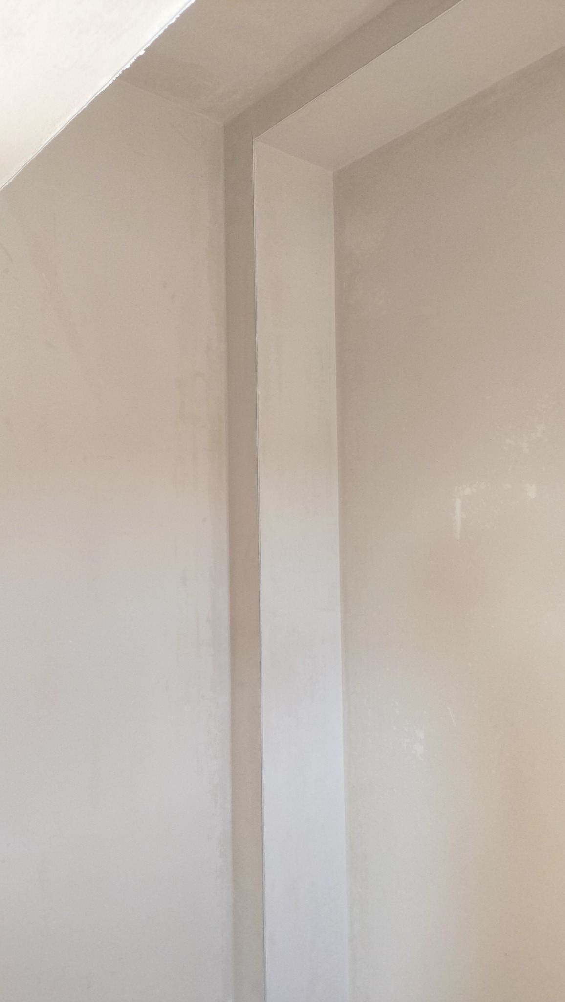 Wnętrze w trakcie prac wykończeniowych: fragment ściany z nałożoną warstwą gładzi, widoczne nierówności i ślady po szpachlowaniu, przygotowane do dalszej obróbki.