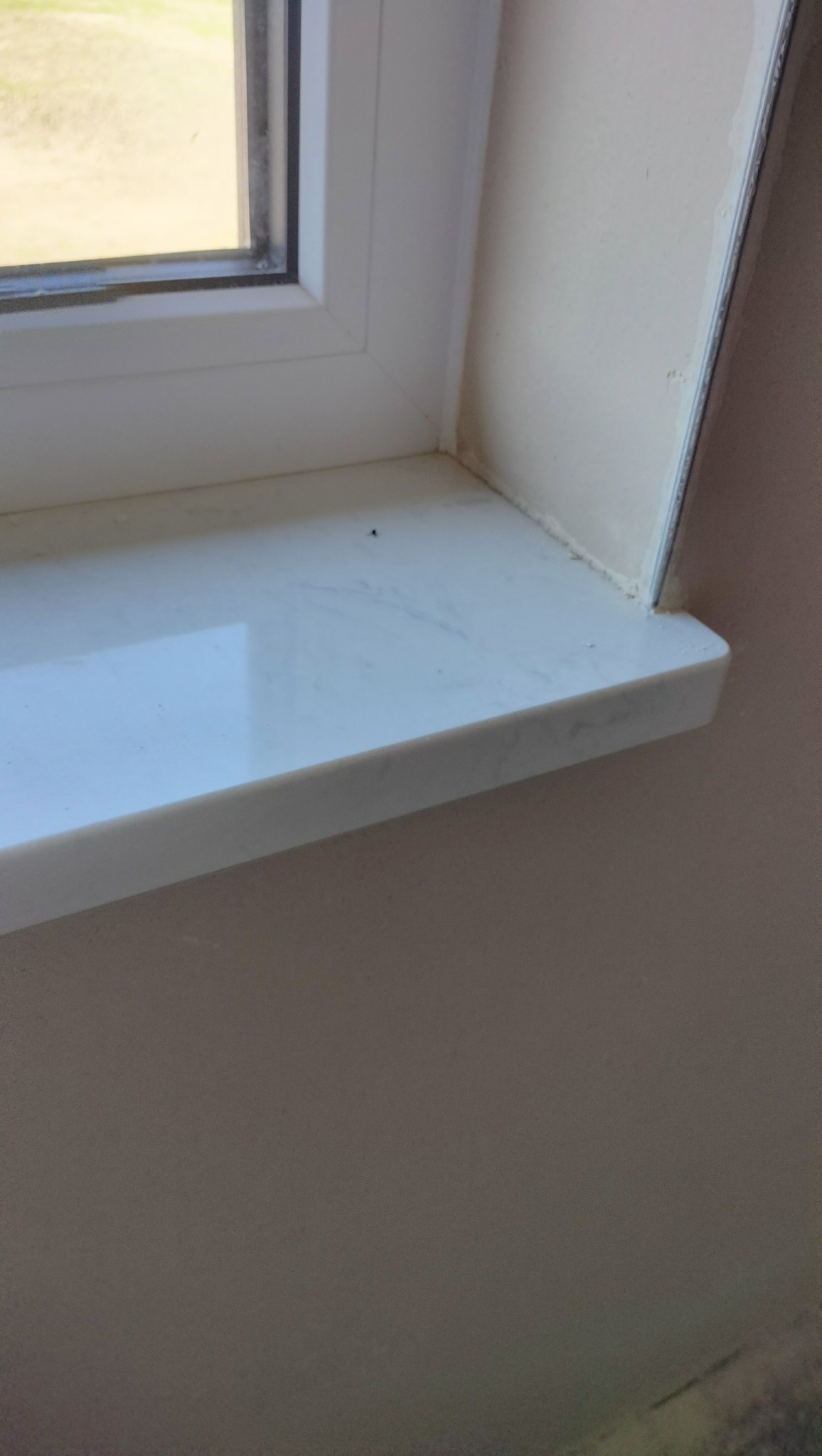 Biały parapet z PCV zamontowany w oknie, ściana pomalowana na beżowo, widoczne ślady po uszczelnianiu silikonem.