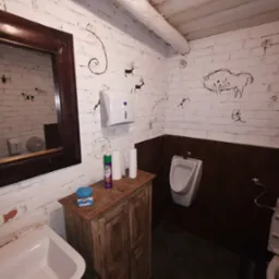 Nietypowa łazienka z białymi cegłami ozdobionymi rysunkami naskalnymi zwierząt, drewnianą szafką pod umywalką i lustrem w ciemnej ramie.