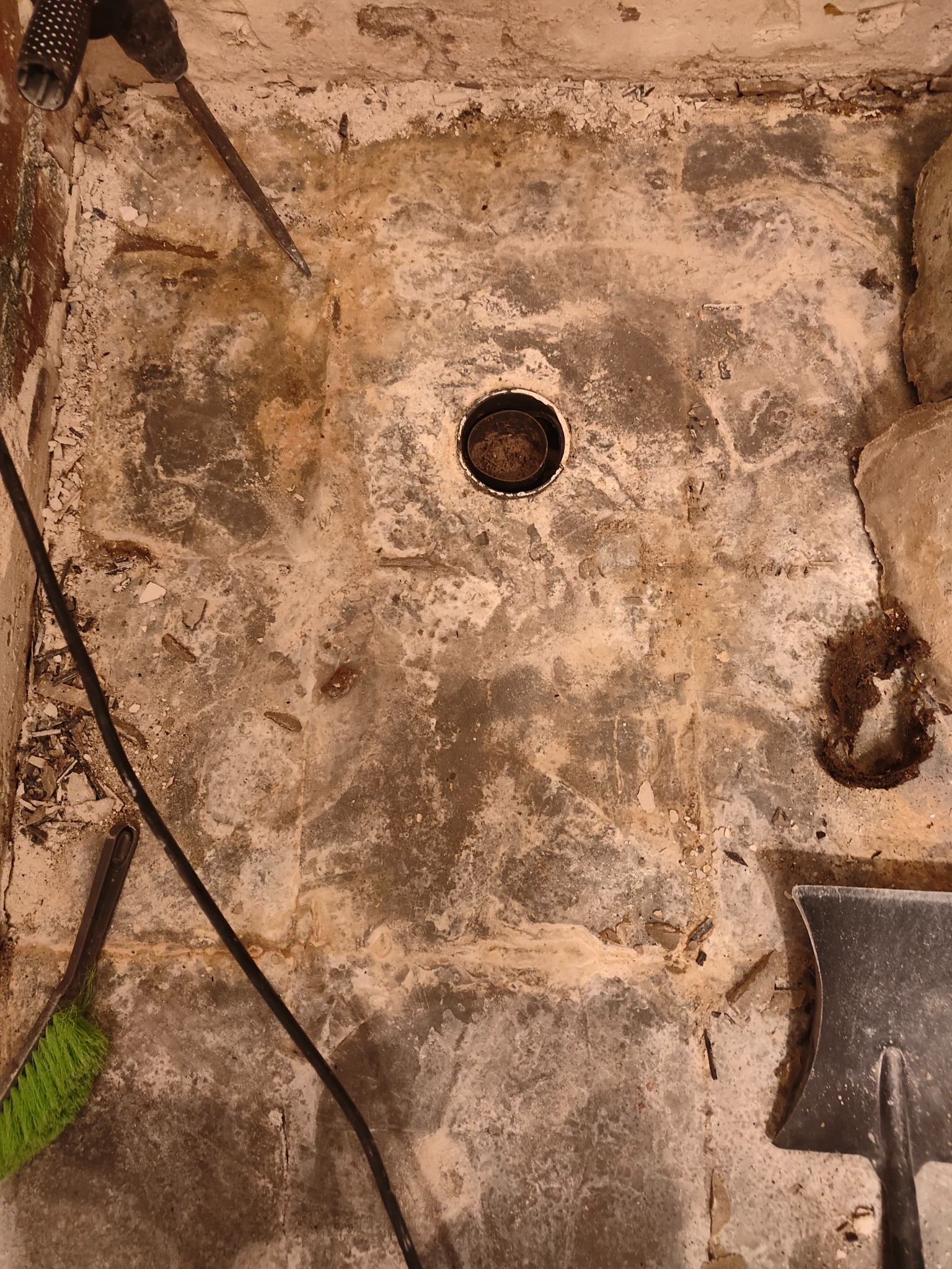 Zdemontowana podłoga w łazience z widocznym odpływem, resztkami kleju i gruzu, przygotowana do dalszych prac remontowych.