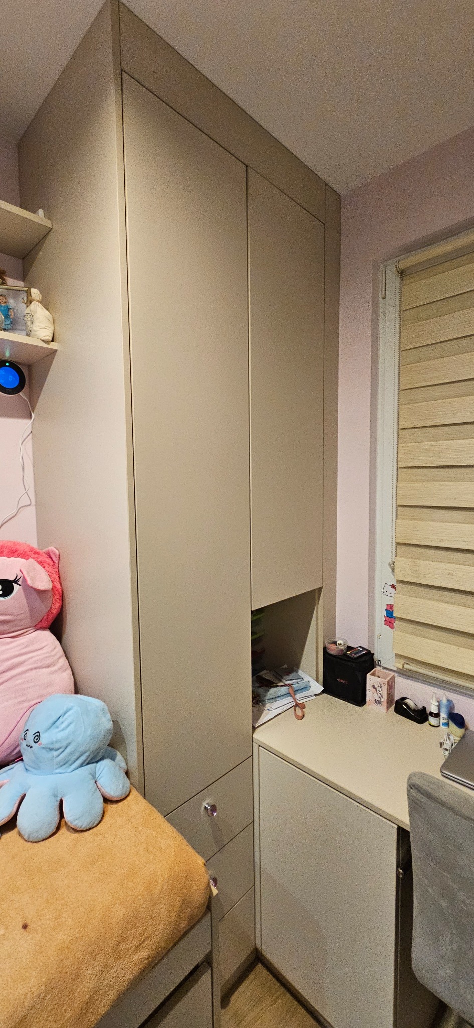 Beżowa szafa na wymiar zintegrowana z biurkiem w pokoju dziecięcym, widoczne pluszaki na łóżku i akcesoria na biurku.