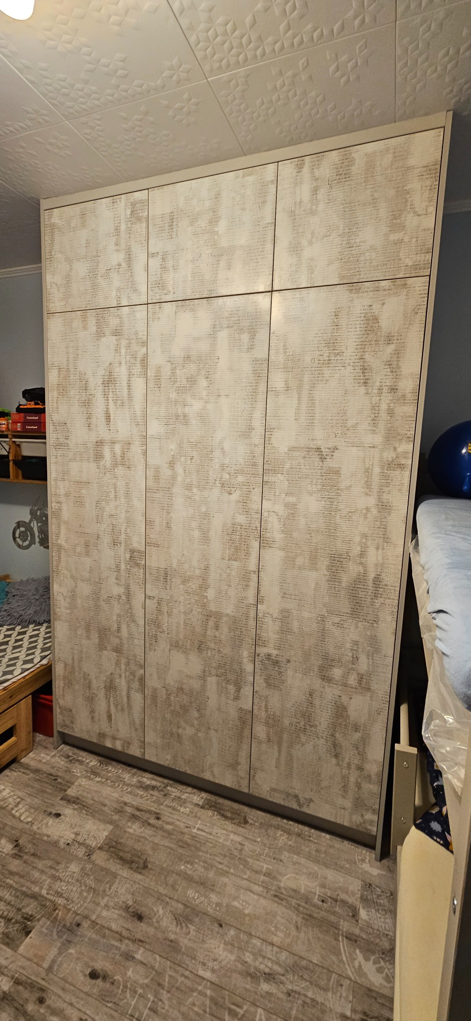 Trzydrzwiowa szafa w odcieniach beżu z intrygującym wzorem na frontach, zamontowana w Bielsku-Białej, widoczna na tle wzorzystego sufitu i drewnopodobnej podłogi.
