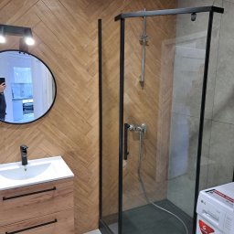 Usługi budowlane Rafał Jaśkowski ROZI - Nowoczesna łazienka z kabiną prysznicową z czarnymi profilami, umywalką z szafką z drewnopodobnym frontem ułożonym w jodełkę, okrągłym lustrem z oświetleniem i pralką LG w rogu