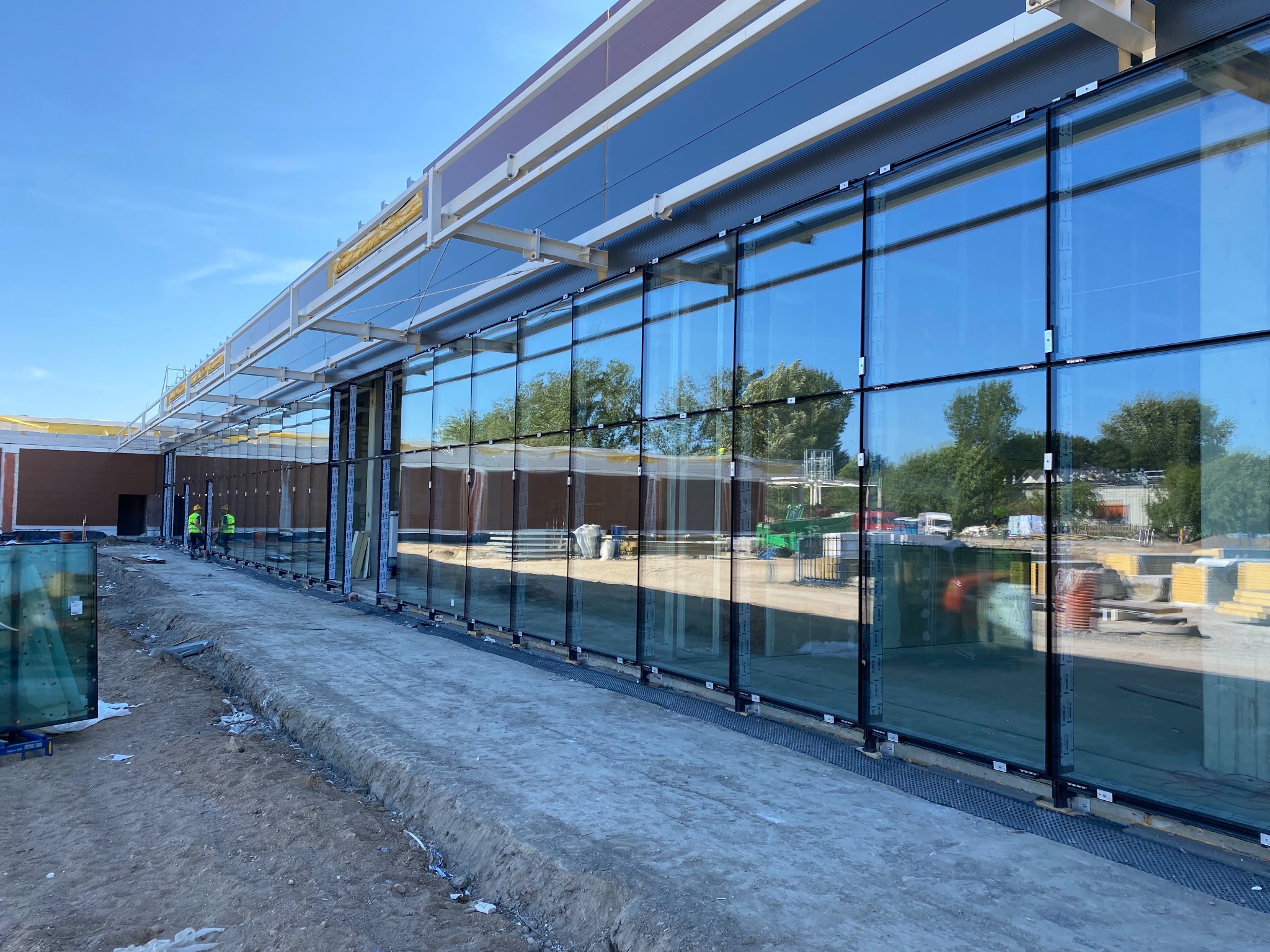 Montaż wielkoformatowych okien aluminiowych na elewacji budynku, widoczni pracownicy w odblaskowych kamizelkach, teren budowy.