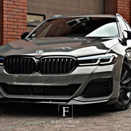 Fura na błysk - Szary, luksusowy samochód BMW po detailingu, z wyraźnie widocznymi detalami karoserii i czarnymi felgami, zaparkowany na tle ceglanej ściany i bramy garażowej.
